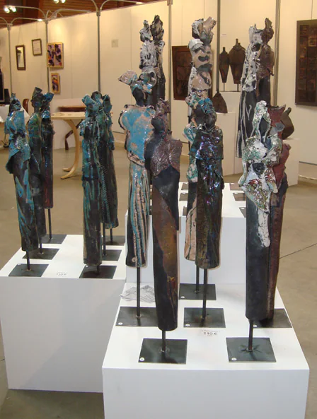 Hautes figures en céramique sombre dressées sur des socles blancs.