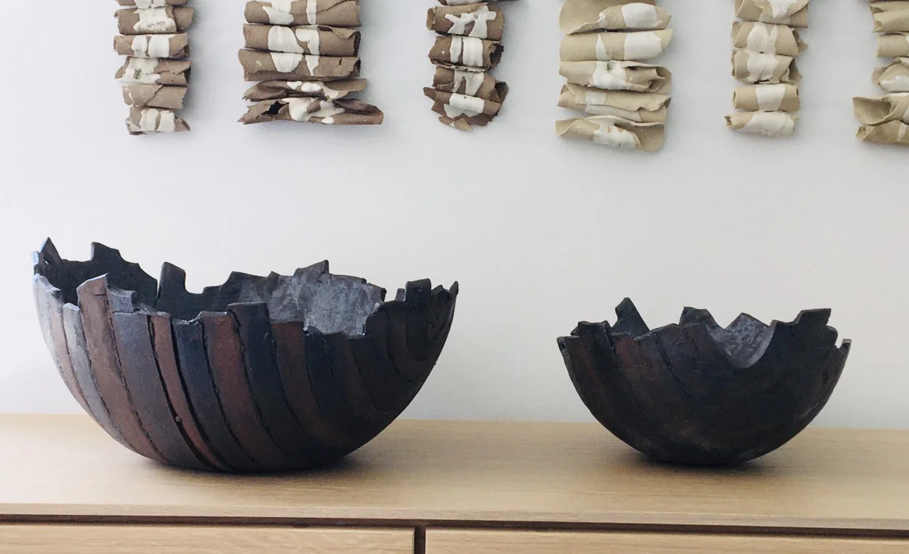 Deux coupes en céramique noire aux bords déchirés, sous une rangée de petites pièces.
