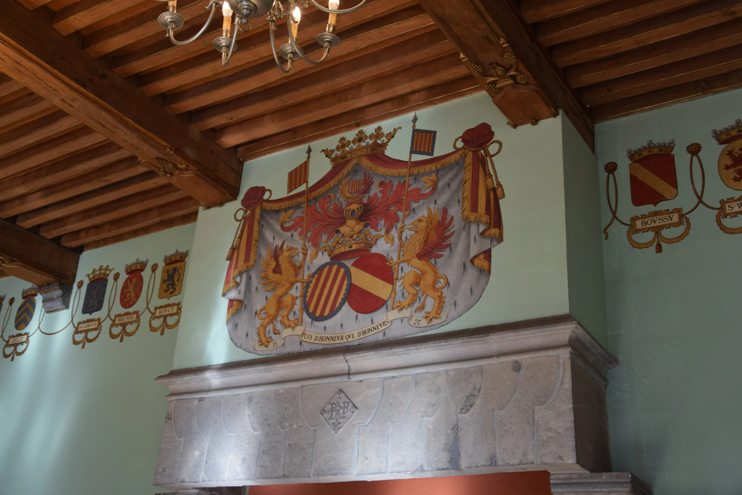 Une cheminée de pierre surmontée d'un grand blason peint, sous un plafond de poutres.