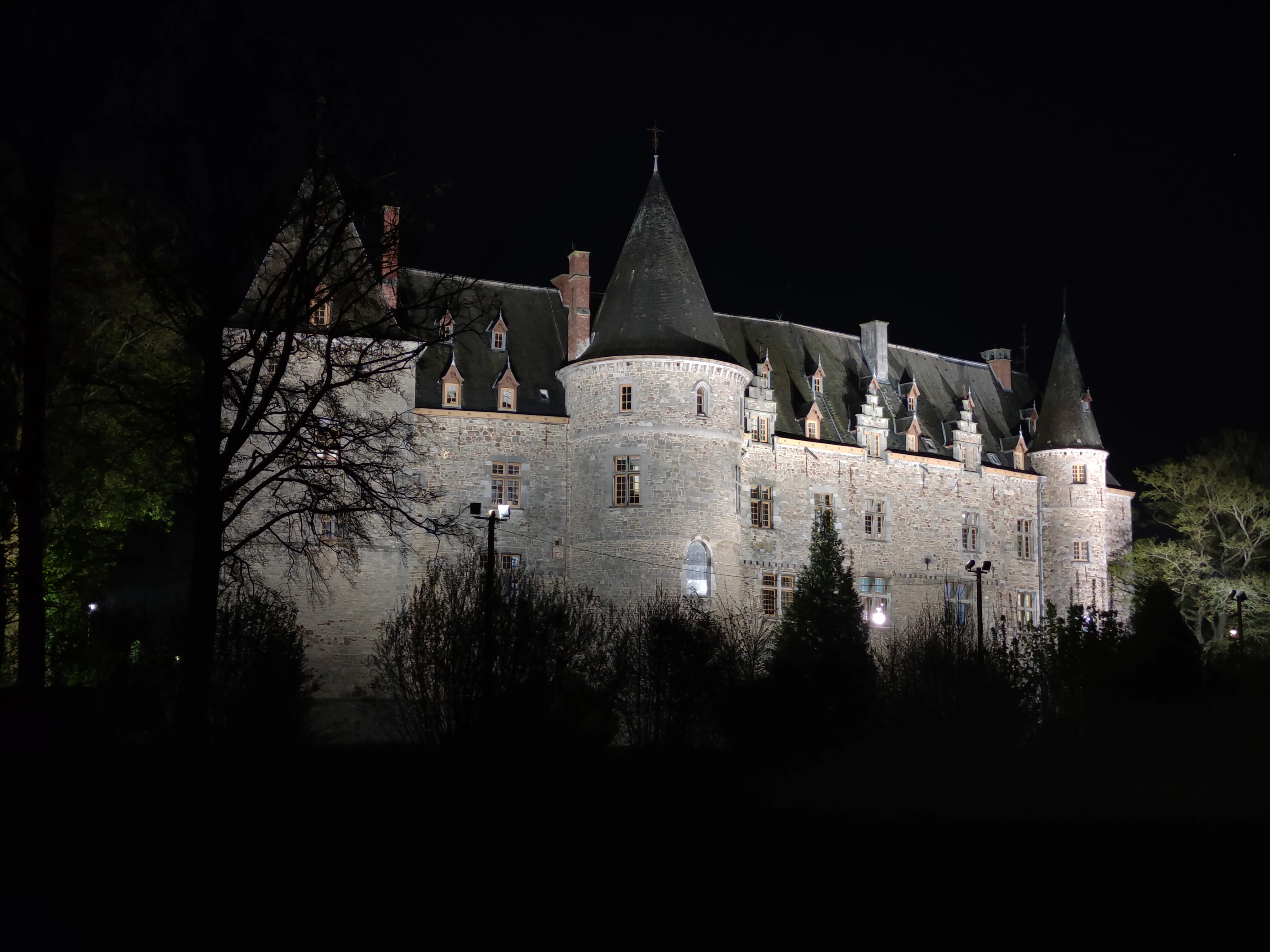Le château d'Ham-sur-Heure illuminé dans la nuit, sa tour ronde coiffée d'une flèche d'ardoise.
