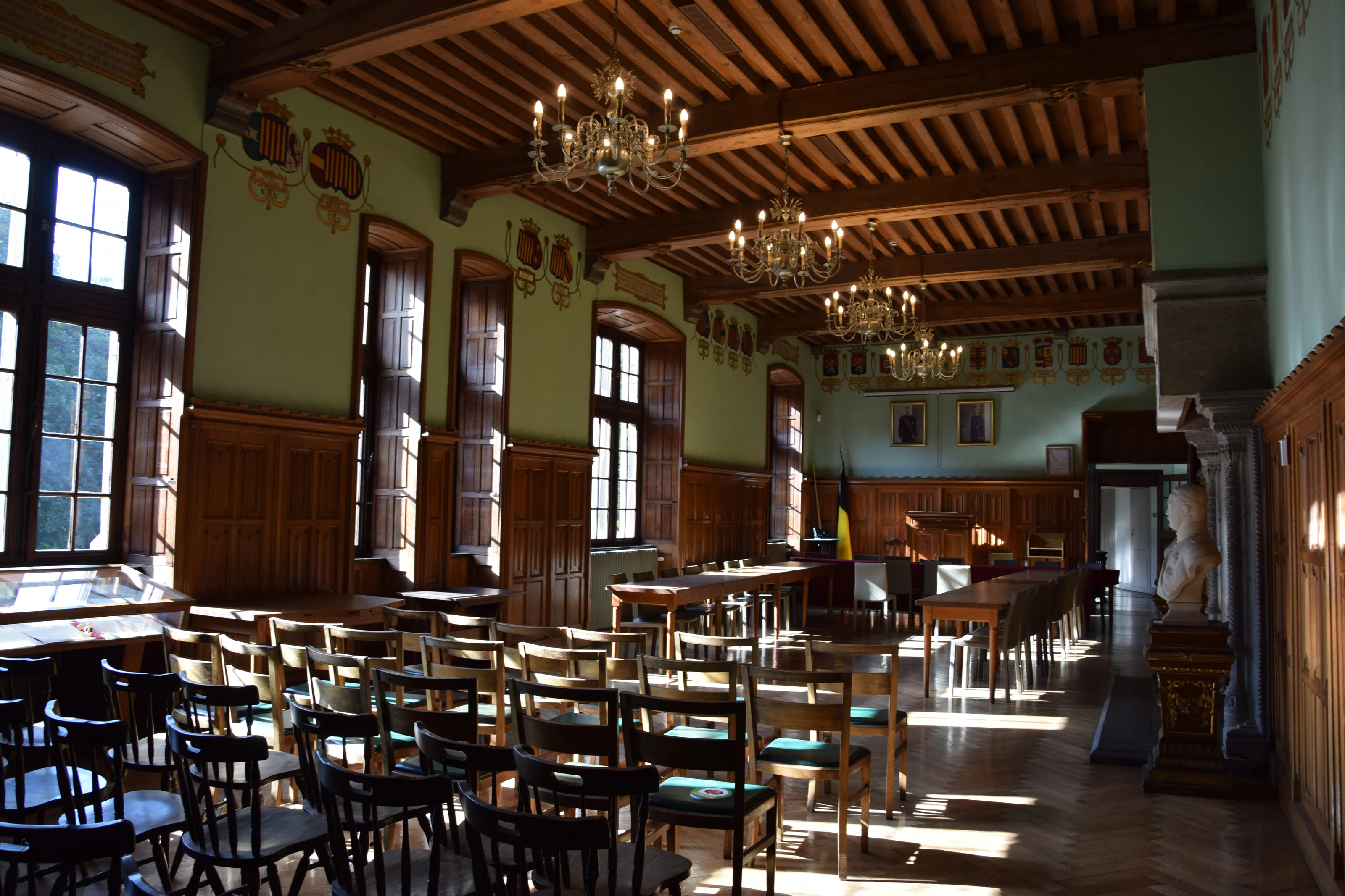 La salle des blasons, son plafond de bois, ses lustres, ses écus peints et le soleil sur le parquet.
