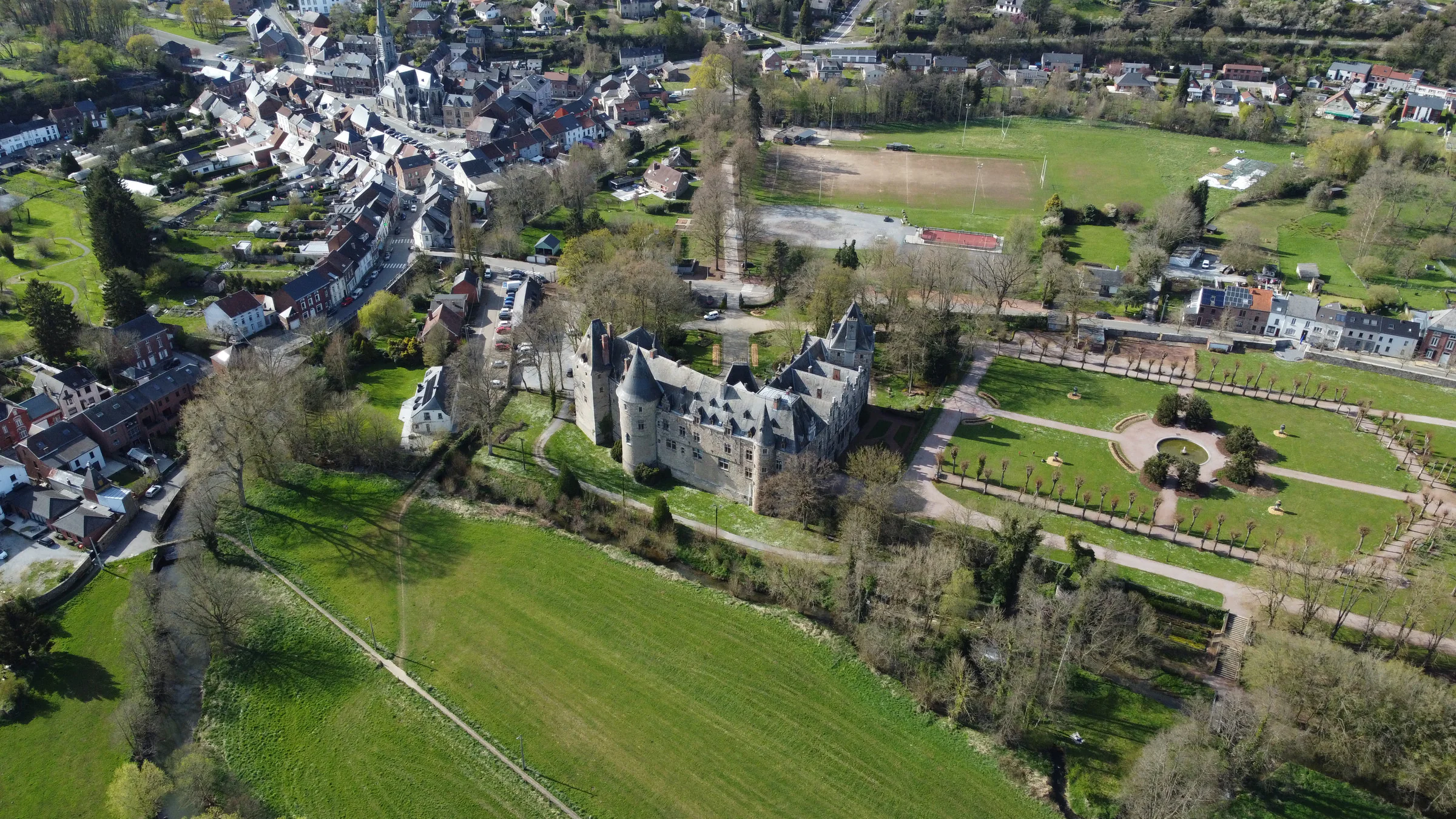Le château vu du ciel, ses deux ailes en équerre au milieu des arbres.