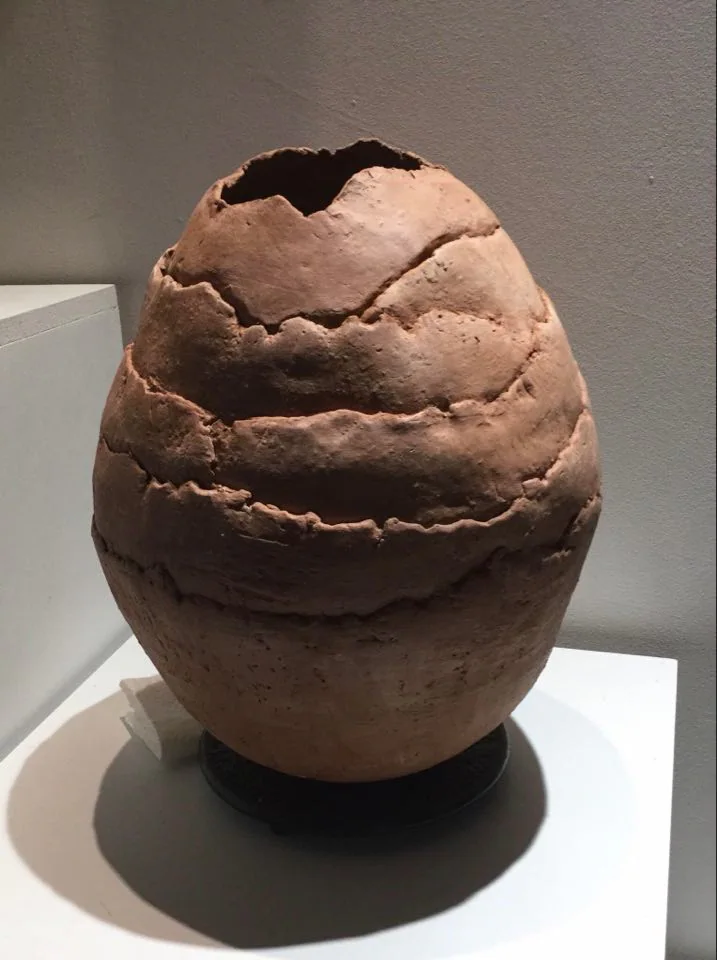 Un vase ovoïde en terre brune, au col ouvert et irrégulier.