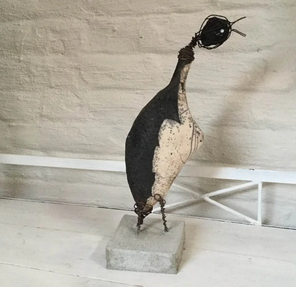 Un oiseau en céramique noire au long bec, sur un socle.